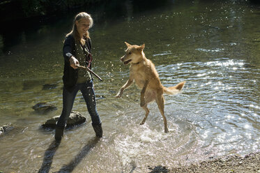 Junge Frau spielt mit ihrem Hund in der Natur - CRF002719