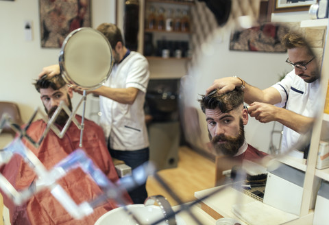 Spiegelung eines Friseurs, der einem Kunden die Haare schneidet, lizenzfreies Stockfoto
