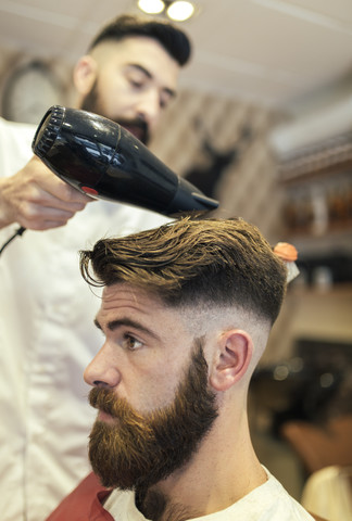 Friseur föhnt das Haar eines Kunden, lizenzfreies Stockfoto
