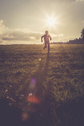 Silhouette eines Jungen, der auf einer Wiese im Gegenlicht läuft - SARF002233