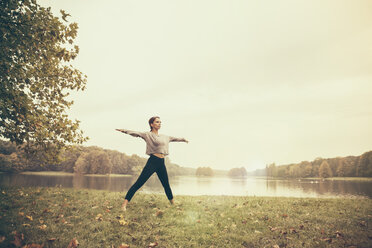 Woman doing a moon salutation yoga pose in autmny park - MFF002440