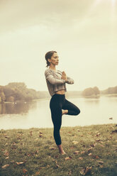 Woman holding a Vrksasana yoga pose in autmny park - MFF002442