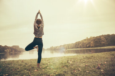 Woman holding a Vrksasana yoga pose in autmny park - MFF002443