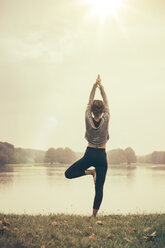 Frau in Vrksasana-Yogastellung im Autmny Park - MFF002444