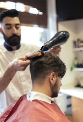 Friseurin föhnt und bürstet das Haar eines Kunden - MGOF000924