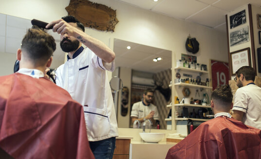 Zwei Friseure schneiden die Haare von Zwillingsbrüdern im Friseursalon - MGOF000927