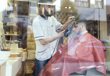 Friseur föhnt das Haar eines Kunden in einem Friseursalon - MGOF000928
