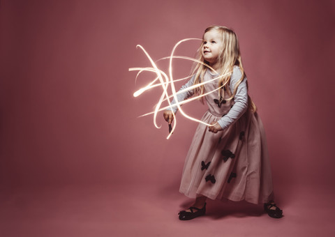 Little girl lightpainting with a torch in front of a pink background stock photo