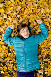Lächelndes Mädchen auf dem mit Herbstblättern bedeckten Boden liegend - LVF004043