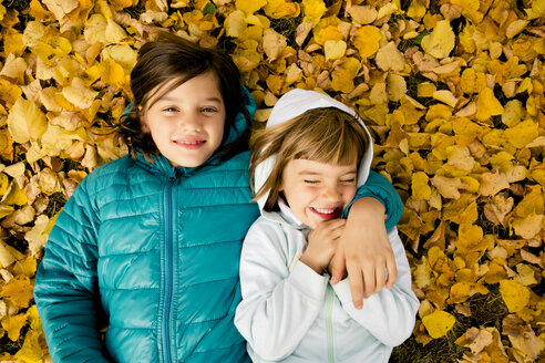 Zwei Mädchen liegen nebeneinander auf dem mit Herbstblättern bedeckten Boden - LVF004044