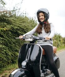 Portrait of smiling girl sitting on a black Vespa - MGOF000935