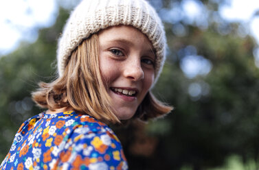 Porträt eines lächelnden Mädchens mit Wollmütze, das über ihre Schulter schaut - MGOF000947