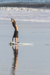 Indonesien, Bali, Surfer beim Dehnen am Strand - KNTF000134
