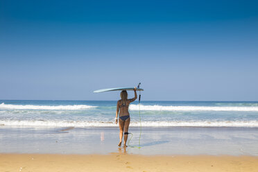 Indonesien, Bali, Rückenansicht einer Frau, die ihr Surfbrett auf dem Kopf trägt, am Strand - KNTF000138