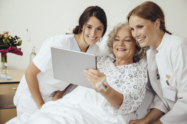 Ältere Frau im Krankenhaus zeigt Arzt und Krankenschwester etwas auf einem digitalen Tablet - MFF002467