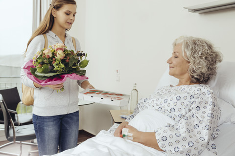 Granddaughter visiting grandmother in hospital, bringing bunch of flowers stock photo