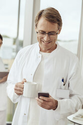 Doctor with coffee cup and smartphone - MFF002480
