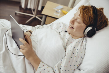 Ein kranker Junge liegt im Krankenhaus und benutzt ein digitales Tablet, während er Kopfhörer trägt - MFF002490