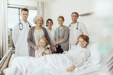 Ärzte und Familienangehörige im Krankenhaus stehen am Bett eines kranken Jungen - MFF002497