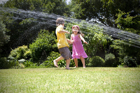 Zwei kleine Kinder spielen mit Rasensprenger im Garten - RMAF000030
