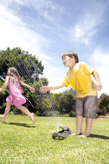 Zwei kleine Kinder spielen mit Rasensprenger im Garten - RMAF000032