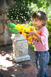 Porträt eines lächelnden kleinen Mädchens, das mit einer Wasserpistole spielt - RMAF000046