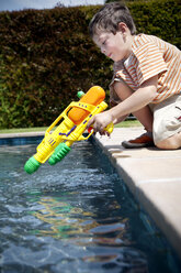 Little boy kneeling with his water gun at pool edge - RMAF000055