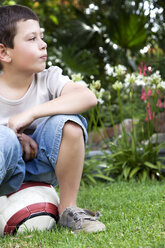 Kleiner Junge sitzt auf einem Fußball im Garten - RMAF000067