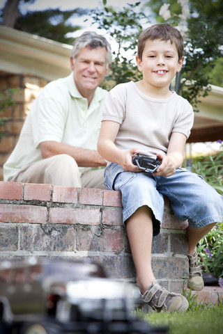 Kleiner Junge spielt mit Spielzeugauto, während sein Großvater im Hintergrund zuschaut, lizenzfreies Stockfoto