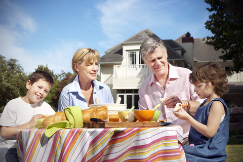 Kleiner Junge und Mädchen mit ihren Großeltern am Esstisch im Garten sitzend, lizenzfreies Stockfoto