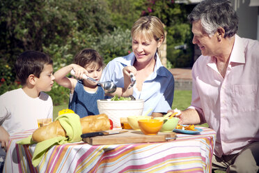 Little boy and girl with their grandparents sitting at dining table in the garden - RMAF000074