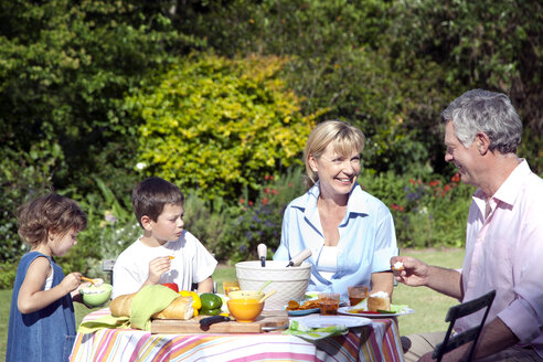 Kleiner Junge und Mädchen mit ihren Großeltern am Esstisch im Garten sitzend - RMAF000076