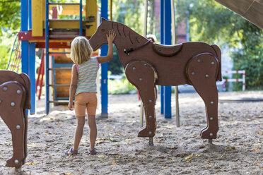 Kleines Mädchen steht auf dem Spielplatz und streichelt ein Holzpferd - JFEF000728