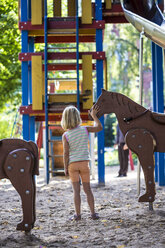 Kleines Mädchen steht auf dem Spielplatz und streichelt ein Holzpferd - JFEF000729