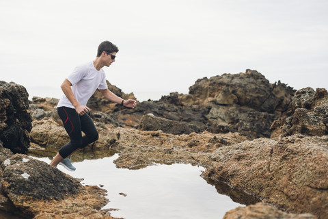 Spanien, Ferrol, Jogger bereit zum Sprung über das Wasser an der Küste, lizenzfreies Stockfoto