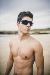 Portrait of shirtless young man on the beach wearing sunglasses - RAEF000581