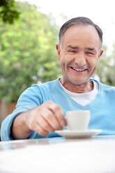 Porträt eines lächelnden reifen Mannes, der mit einer Tasse Kaffee sitzt - RMAF000088