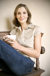 Porträt einer entspannten jungen Frau auf einer Holzbank sitzend mit einer Tasse Cappuccino - RMAF000092