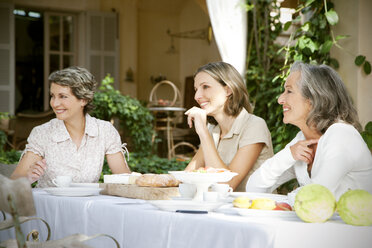 Spanien, Mallorca, drei Freundinnen sitzen am gedeckten Tisch im Garten - RMAF000096