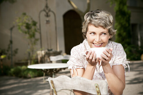 Spain, Mallorca, portrait of smiling mature woman sitting in the garden with cup of Cappuccino - RMAF000100