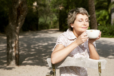 Porträt einer reifen Frau, die im Garten sitzt und eine Tasse Cappuccino trinkt - RMAF000101