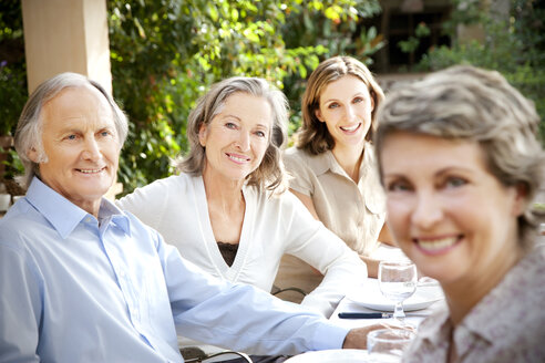 Four smiling friends sitting at laid table in the garden - RMAF000110