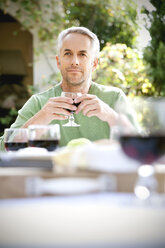 Porträt eines träumenden Mannes, der am gedeckten Tisch im Garten sitzt und ein Glas Rotwein hält - RMAF000114
