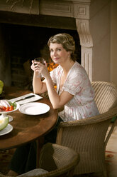 Portrait of smiling mature woman sitting at laid table holding glass of red wine - RMAF000136