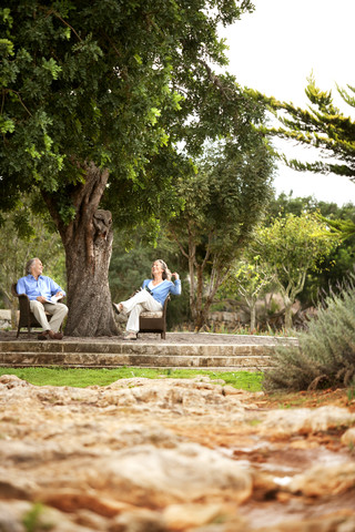 Spanien, Mallorca, Paar entspannt sich unter einem Baum im Garten, lizenzfreies Stockfoto