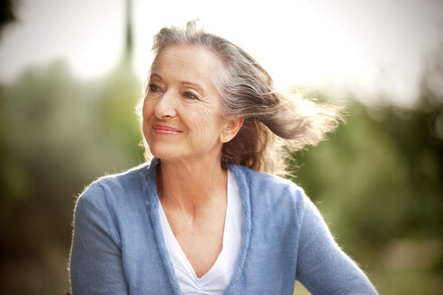 Portrait of smiling woman with blowing hair in the garden - RMAF000148