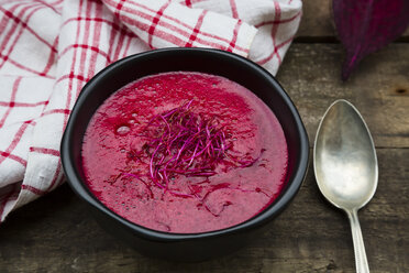 Bowl of beetroot soup garnished with beetroot sprouts on dark wood - LVF004069