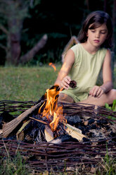 Mädchen sitzt auf einer Wiese hinter einem Lagerfeuer - LVF004080