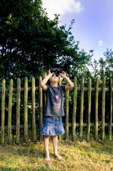 Little girl standing on a meadow watching something with binocular - LVF004081