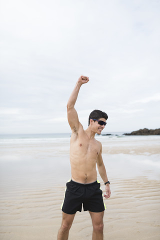 Spain, Galicia, Ferrol, athletic shirtless man on the beach raising his arm stock photo